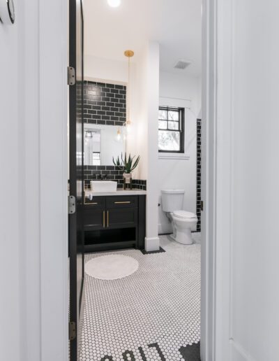 Black and white bathroom with hexagonal floor tiles, black subway wall tiles, a toilet, and a vanity with a mirror and pendant light.