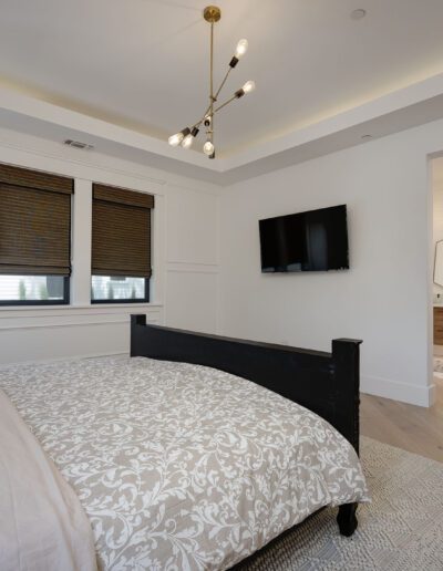 Modern bedroom with a large bed, patterned bedding, ceiling light fixture, wall-mounted TV, and entry to a bathroom.