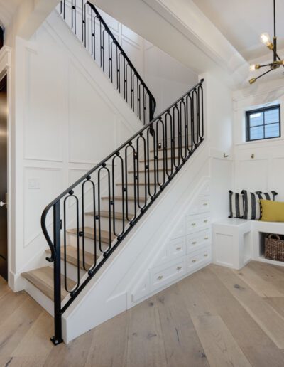 A modern entryway with a staircase featuring black railings, a bench with cushions, storage baskets, and a large wall clock.