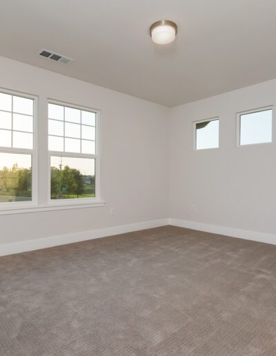 An empty room with beige carpet, white walls, two large windows, and a ceiling light fixture.