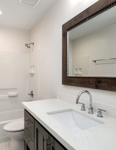 Modern bathroom with a white bathtub and shower, a large mirror above a sink with a marble countertop, and neutral-colored walls.