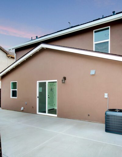 Back view of a brown two-story house with a sliding glass door, patio area, air conditioning unit, and wooden fence.
