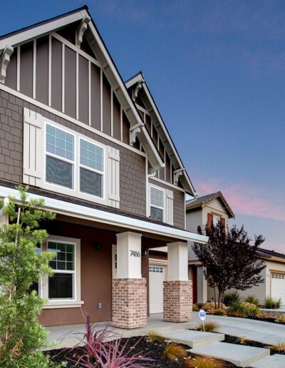 Two-story suburban house with brown exterior, white trim, and front porch. Driveway and small landscaped yard in front.